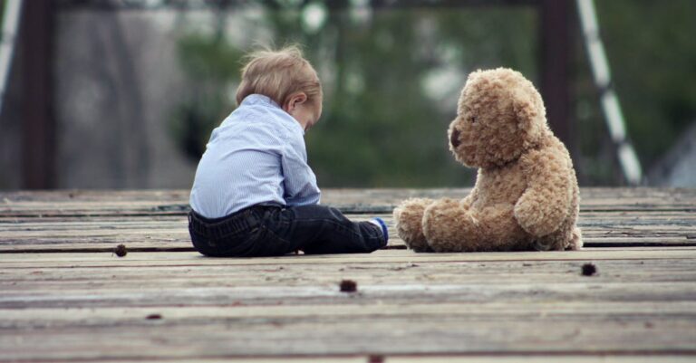 Boy Sitting With Brown Bear Plush Toy on Selective Focus Photo