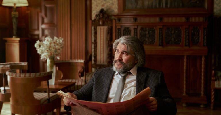 Man Sitting by the Table Holding a Newspaper