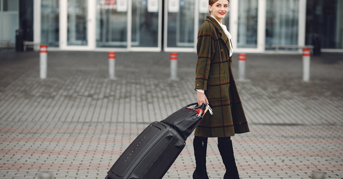 Full length of smiling female manager in stylish coat walking with suitcase and bag while traveling on business trip smiling away