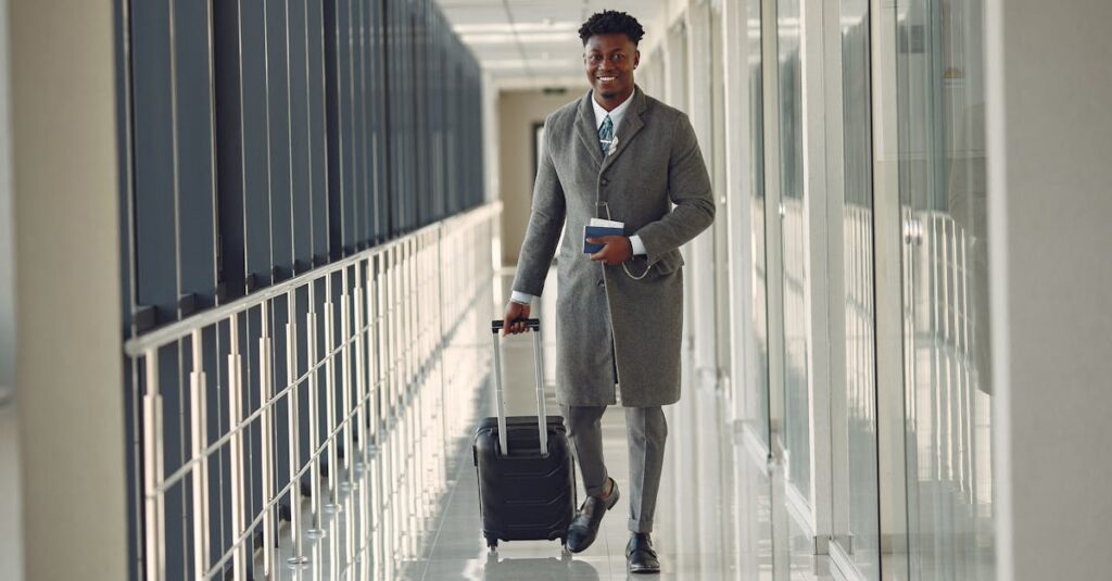 Stylish man with suitcase and passport walking along airport corridor