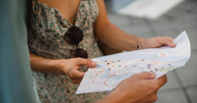 Crop anonymous couple travelers in summer clothes checking location in paper map while walking in unknown city