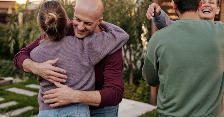 Cheerful friends hugging and smiling while spending time together in suburban yard during weekends