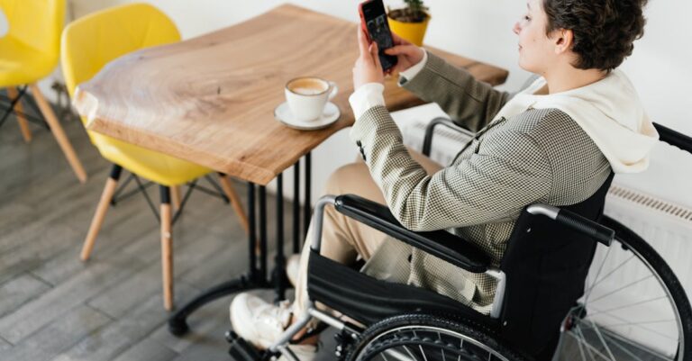 Side view full body of female in wheelchair taking picture of hot coffee while sitting at wooden table in cafeteria