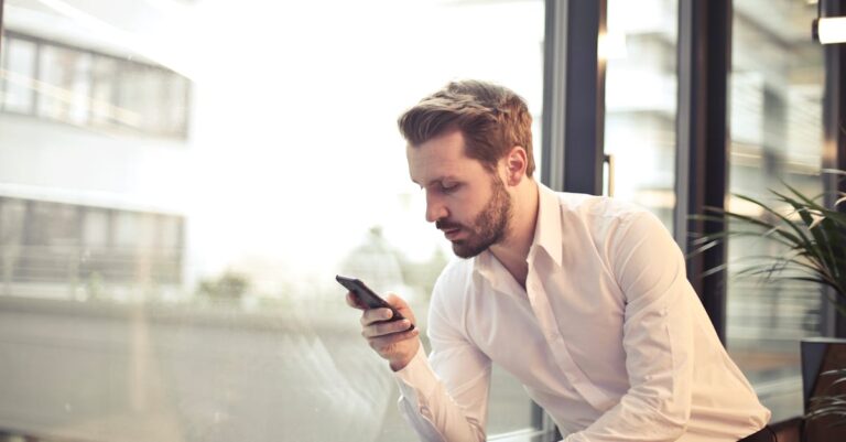 Photo of Man in White Dress Shirt Holding Phone Near Window