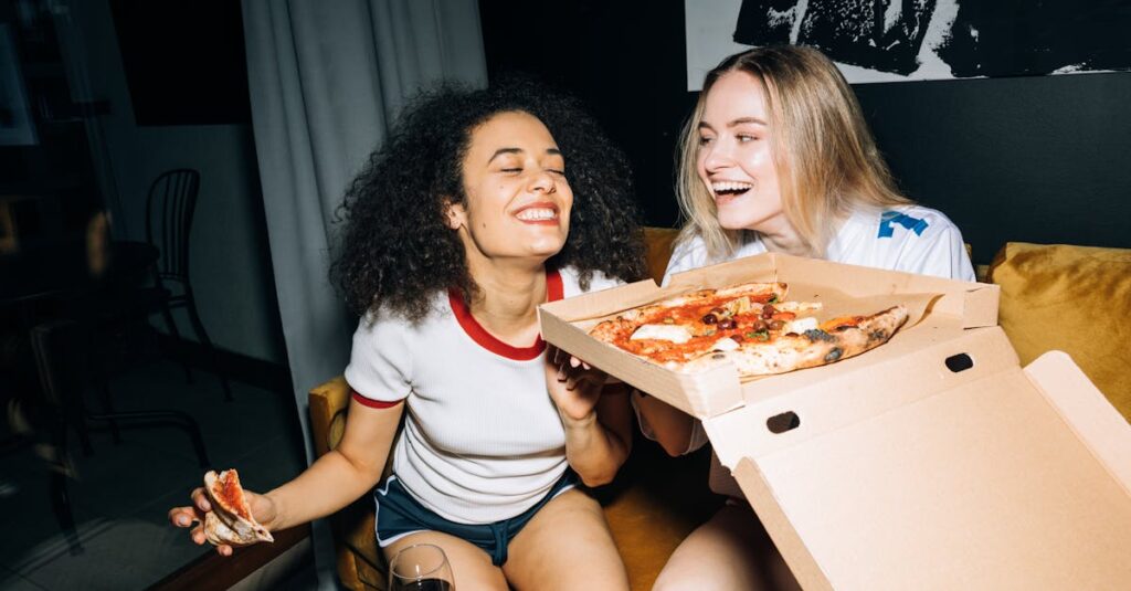 Two happy friends laughing and enjoying pizza indoors during a cozy night in.