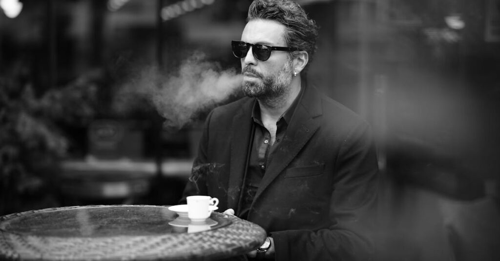 Black and white photo of a well-dressed man smoking at a café, enjoying espresso.