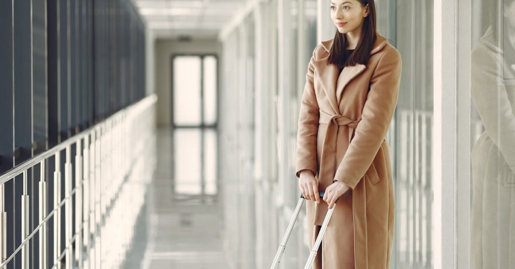 Elegant woman in a beige coat with luggage in a contemporary airport corridor.