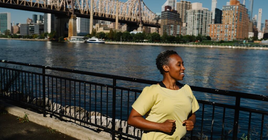 An African American woman jogging near the riverbank with a cityscape in the background.