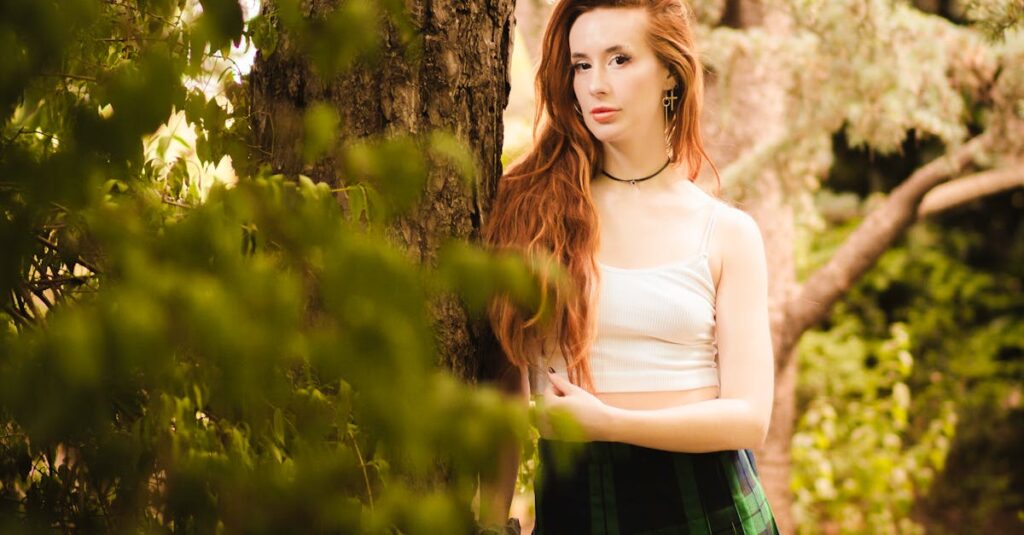 A young woman with long red hair poses by a tree in a lush New York park.