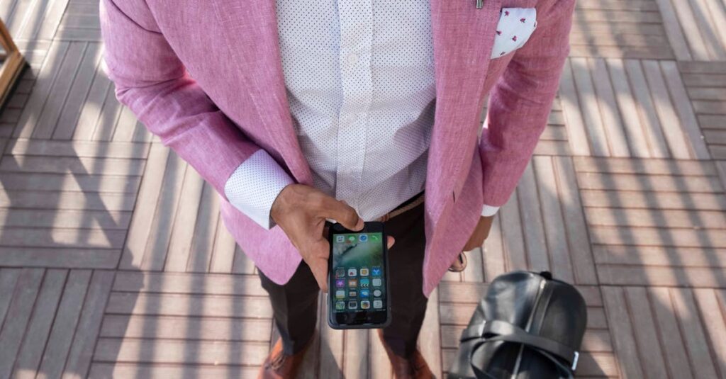 Stylish man in a pink blazer checks his smartphone while traveling with a leather bag.