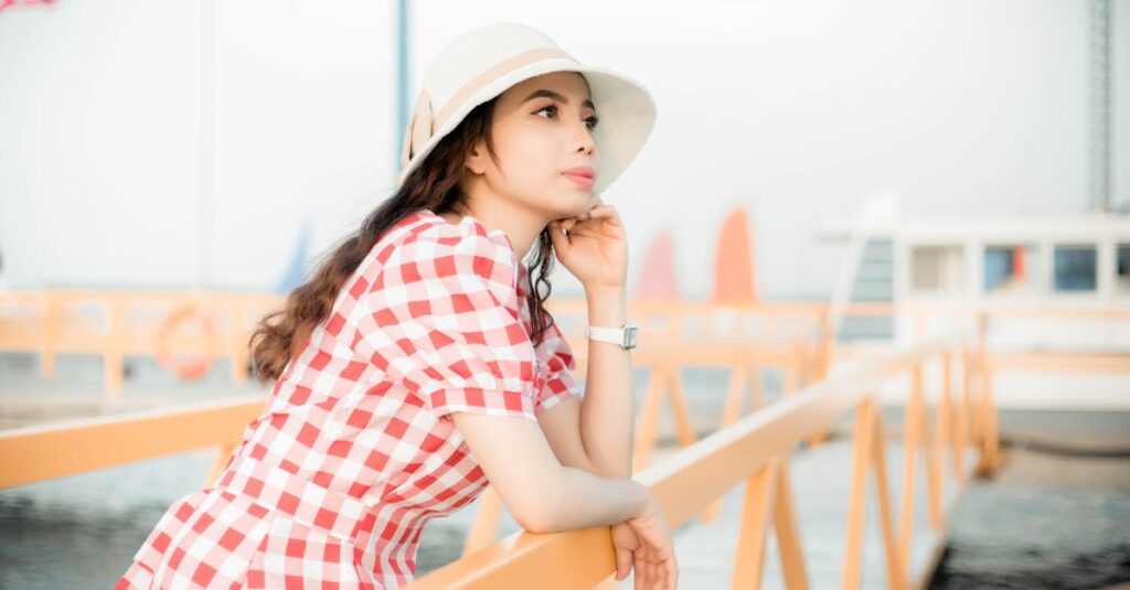 A woman in a red checkered dress and hat enjoys a sunny day on a pier, embodying summer relaxation.