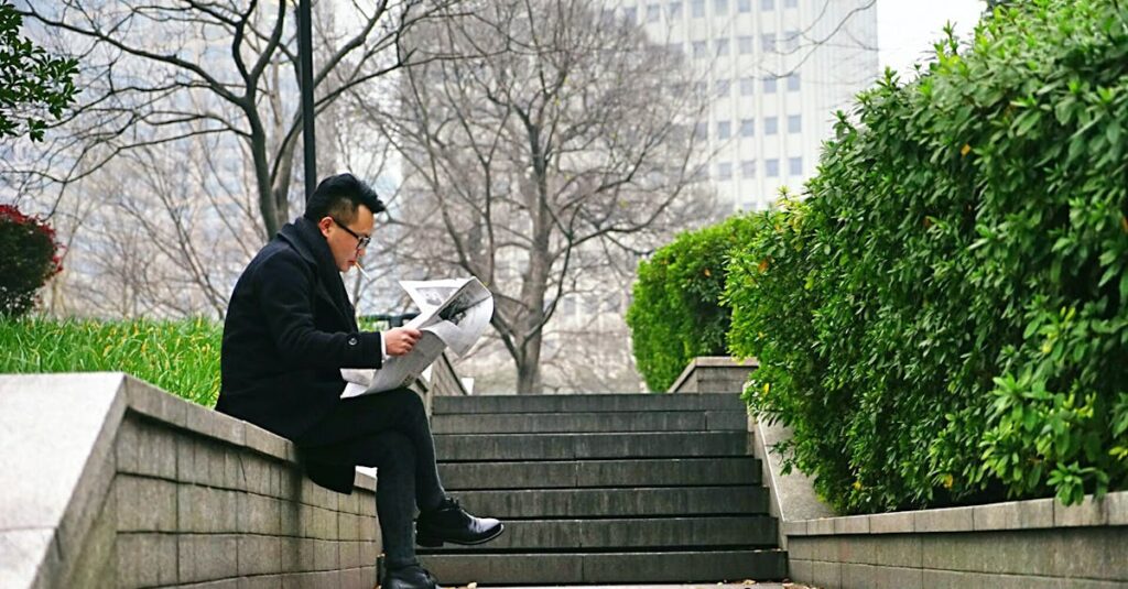 Man reading newspaper outdoors on a park bench during a peaceful afternoon break.