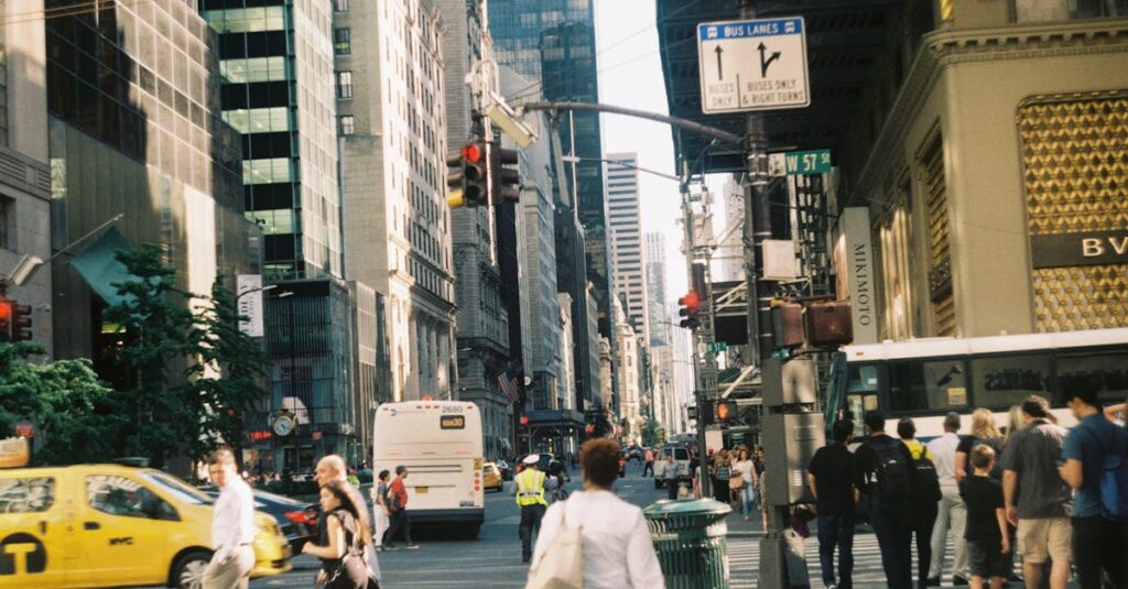 Busy city street with pedestrians, cabs, buses, and tall buildings on a sunny day.