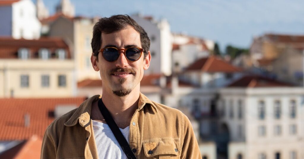 A bearded man smiles while wearing sunglasses against a sunny urban backdrop. Ideal for travel and lifestyle imagery.