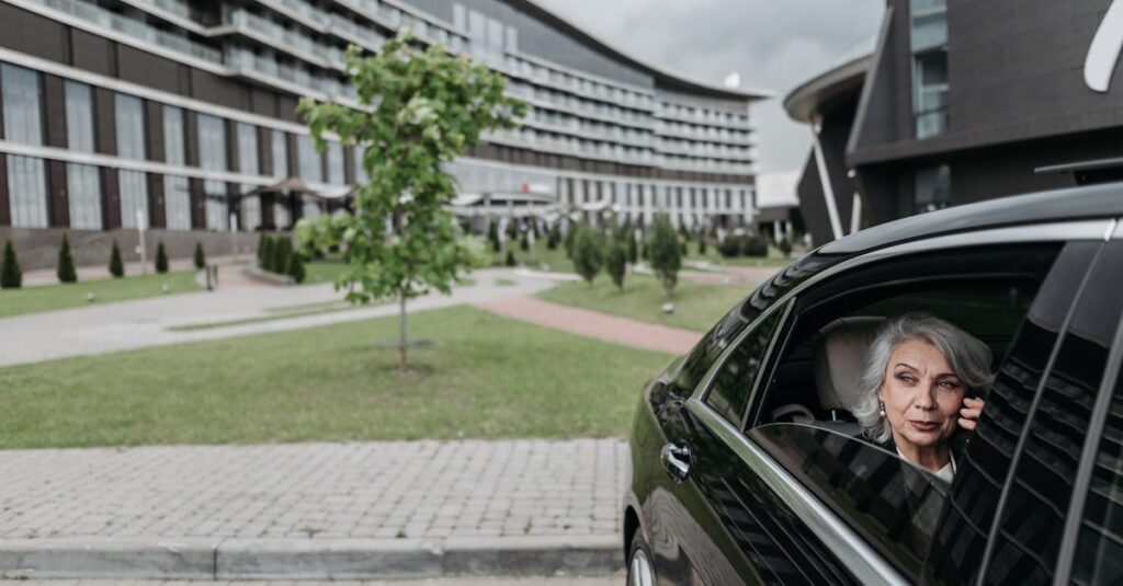 Elderly woman with grey hair on a phone call sitting in car near modern building.